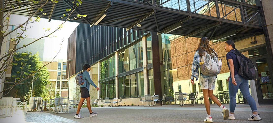 student success district - students walking under walkway bridge of new building